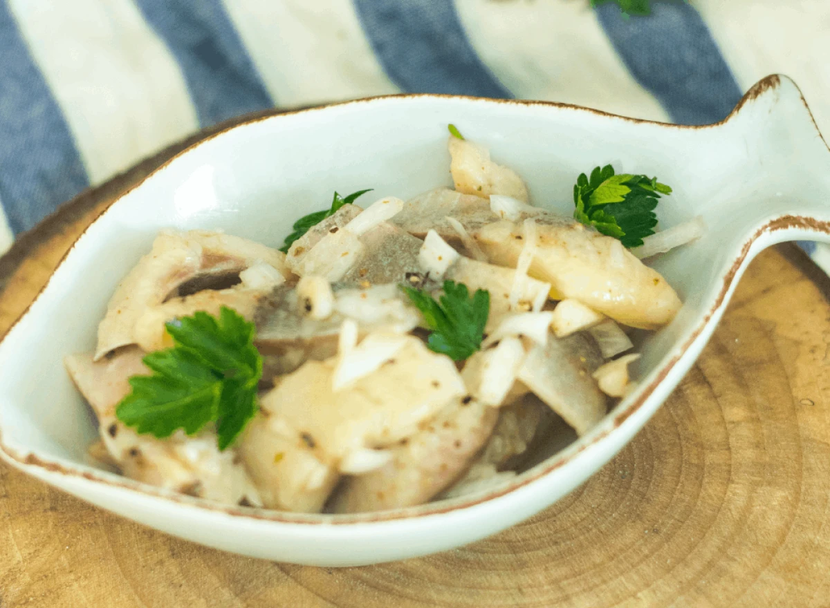 Śledzie w oleju z cebulą podane na talerzu w kształcie ryby